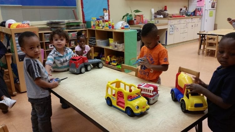 Children at a table playing with toy vehicles.